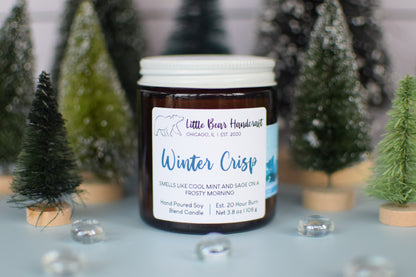 Candle jar labeled 'Winter Crisp' with decorative Christmas trees in the background