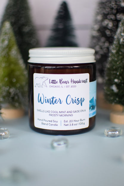 Candle jar labeled 'Winter Crisp' with decorative Christmas trees in the background